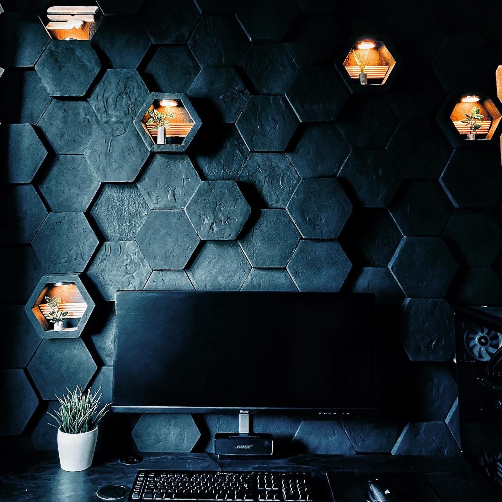 Dunkle Hexagon-Akzentwand mit warm beleuchteten Nischen hinter einem Gaming-Arbeitsplatz