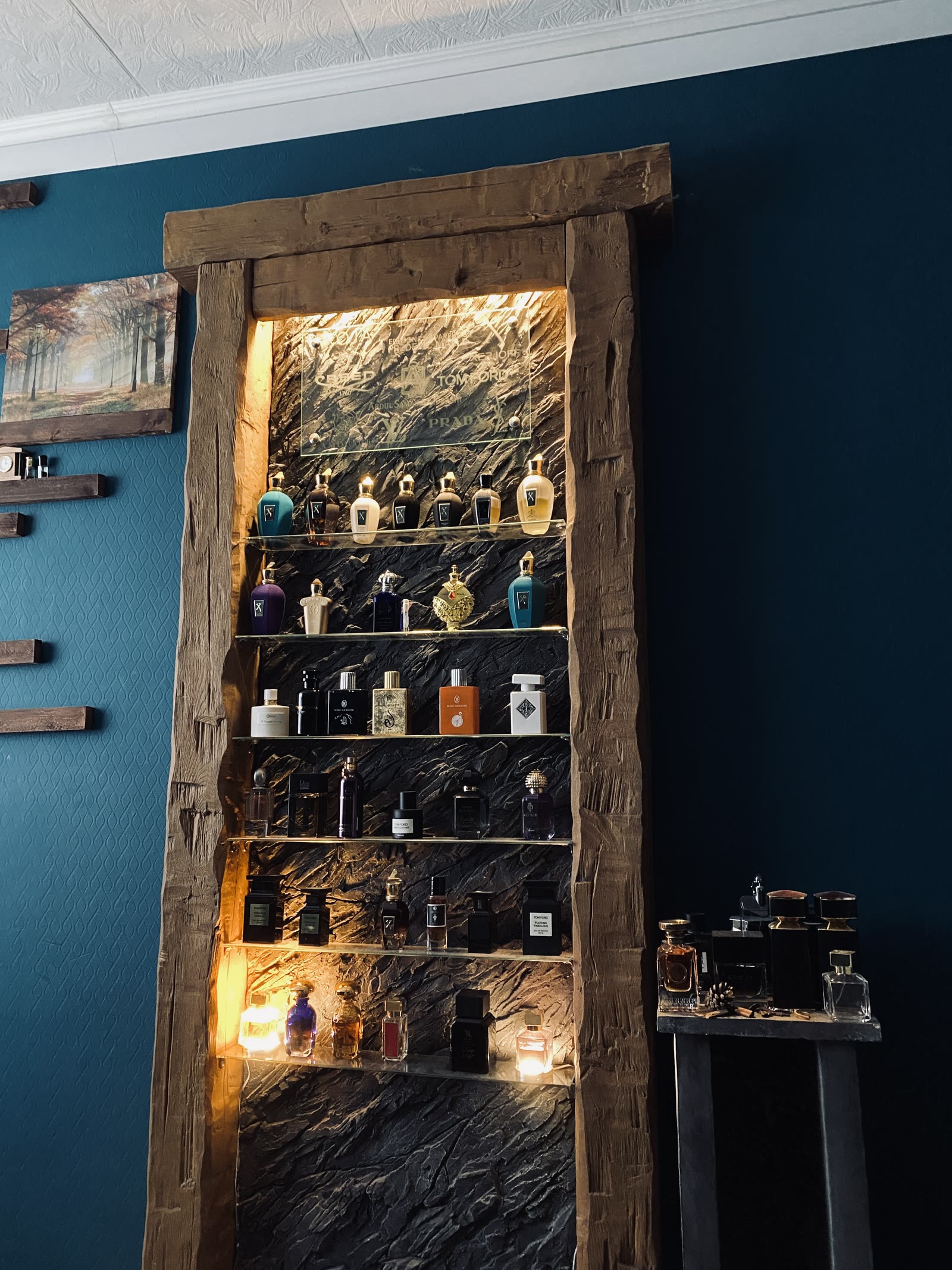Beleuchtetes Parfümregal mit Glasböden vor einer Kunststein-Felsrückwand im rustikalen Holzrahmen