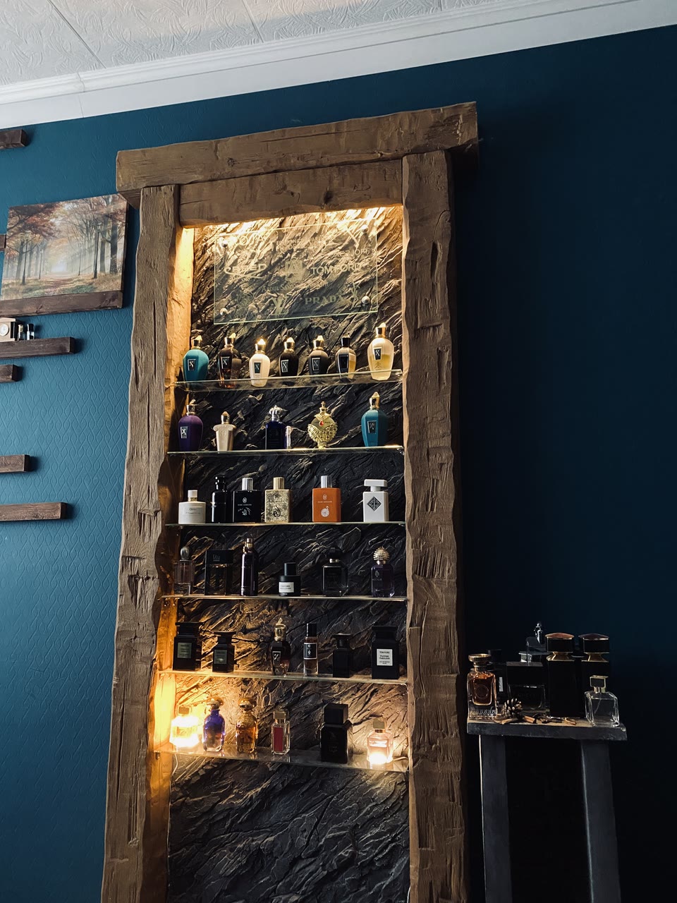 Beleuchtetes Parfümregal mit Glasböden vor einer Kunststein-Felsrückwand im Holzrahmen