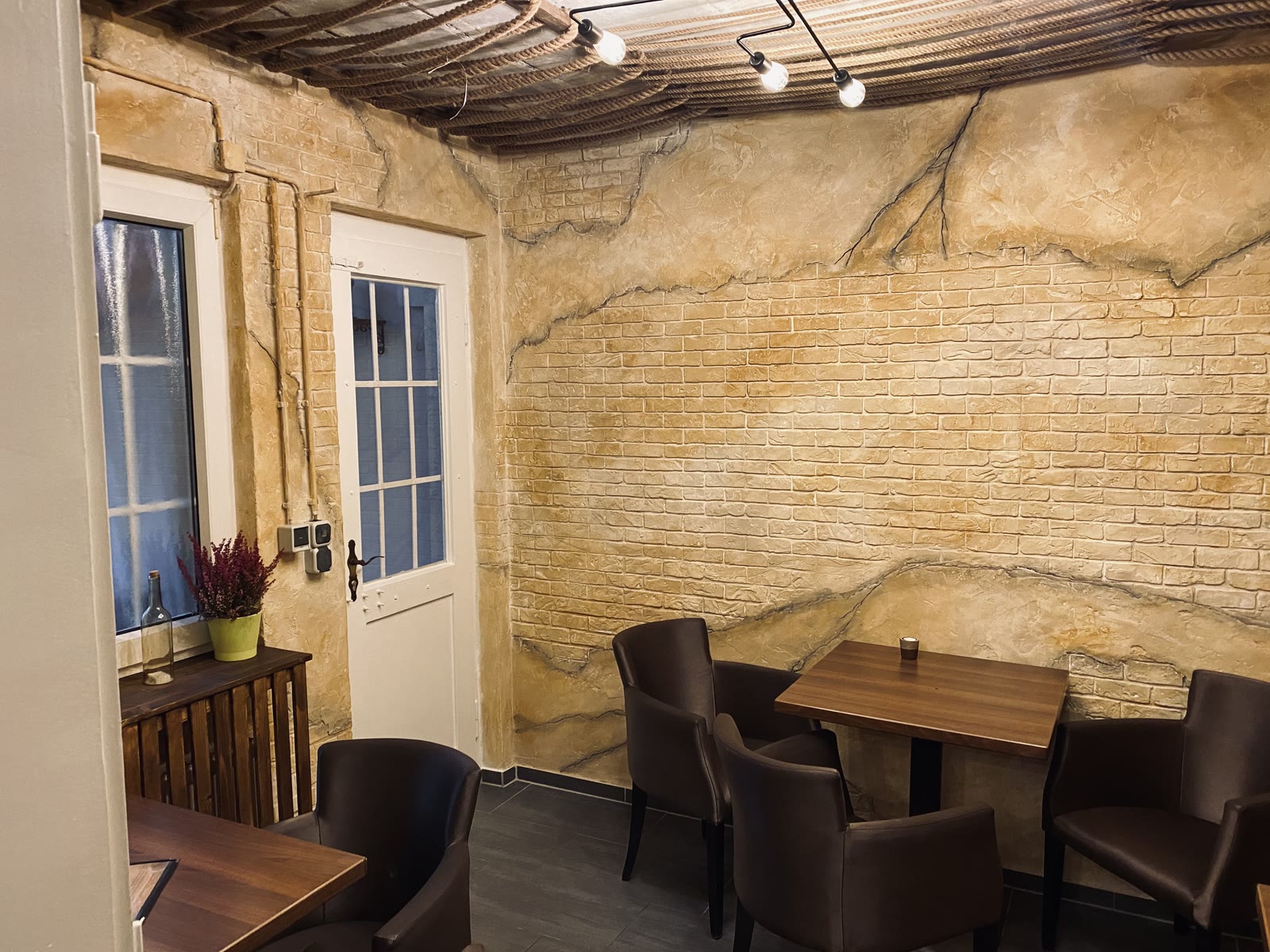 Gastraum mit Kunststein-Wand in Sandstein- und Ziegelsteinoptik, Seildecke, Holztischen und Lederstühlen