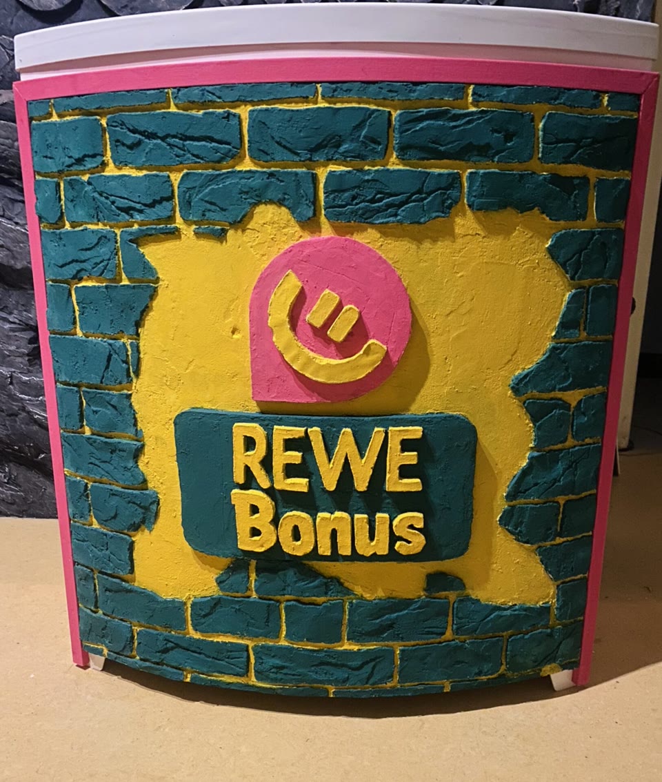 Kunststein-Promotionsstand in Ziegeloptik mit farbigem Relief und Schriftzug „REWE Bonus”