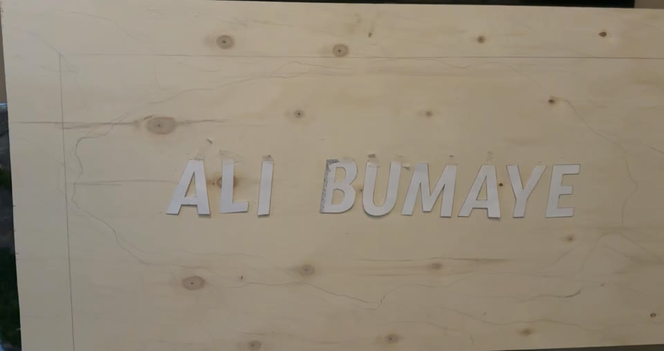 Holzplatte mit vorgezeichneter Felskontur und Papierbuchstaben als Vorlage für den Schriftzug