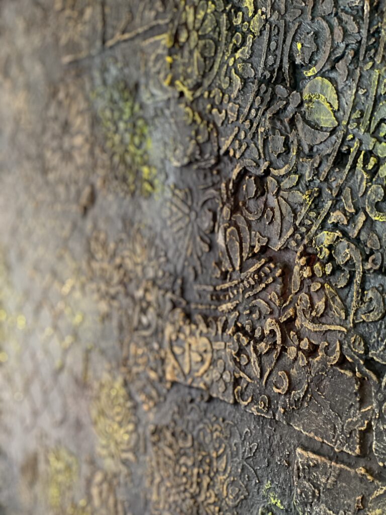 Nahaufnahme einer dunklen Kunststein-Wand mit erhabenen orientalischen Ornamenten, floralen Mustern und gelben Farbakzenten.