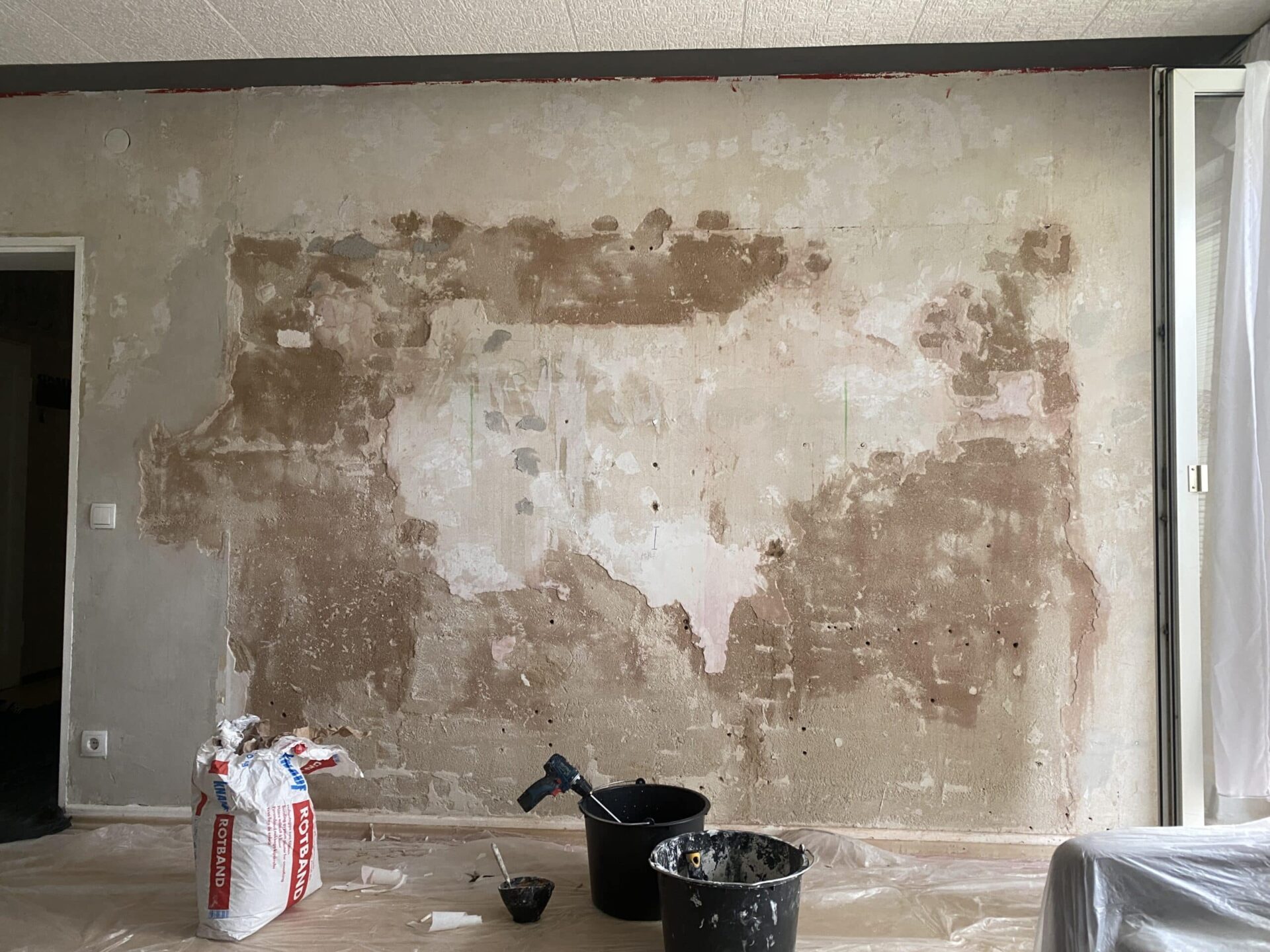 Unverputzte, rohe Wand mit ersten Spachtelarbeiten und Bauutensilien am Boden vor der Neugestaltung.