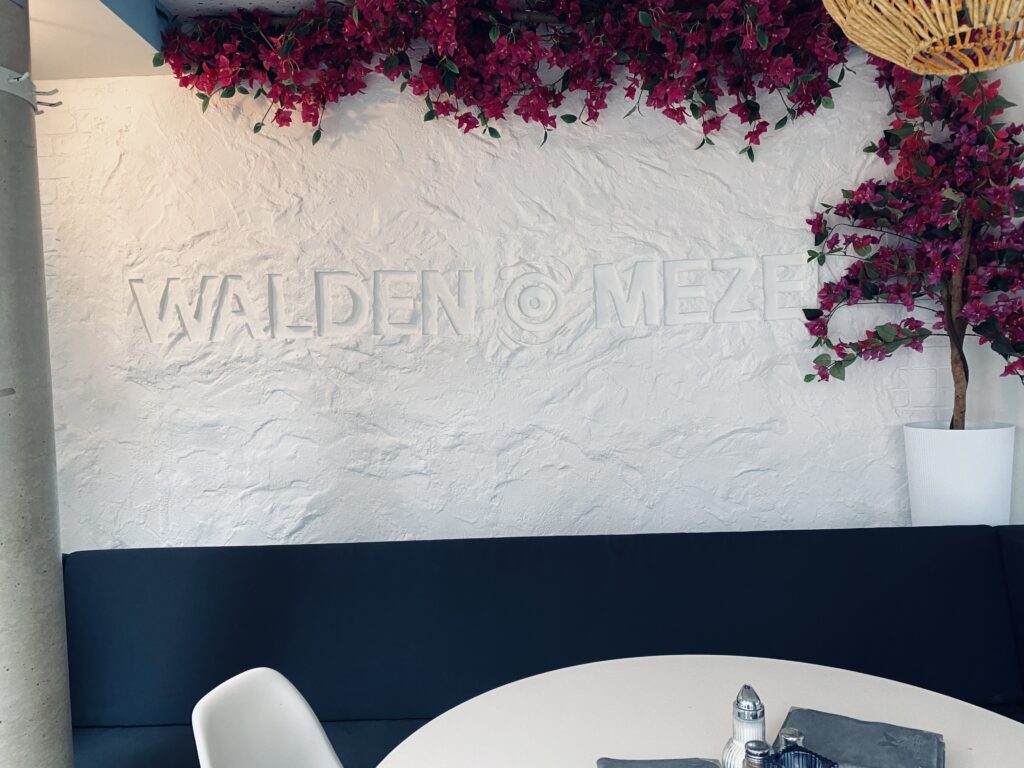 Frontalansicht einer weiß strukturierten Putzwand mit eingearbeitetem Schriftzug-Relief und pinken Bougainvillea-Blüten am oberen Rand.