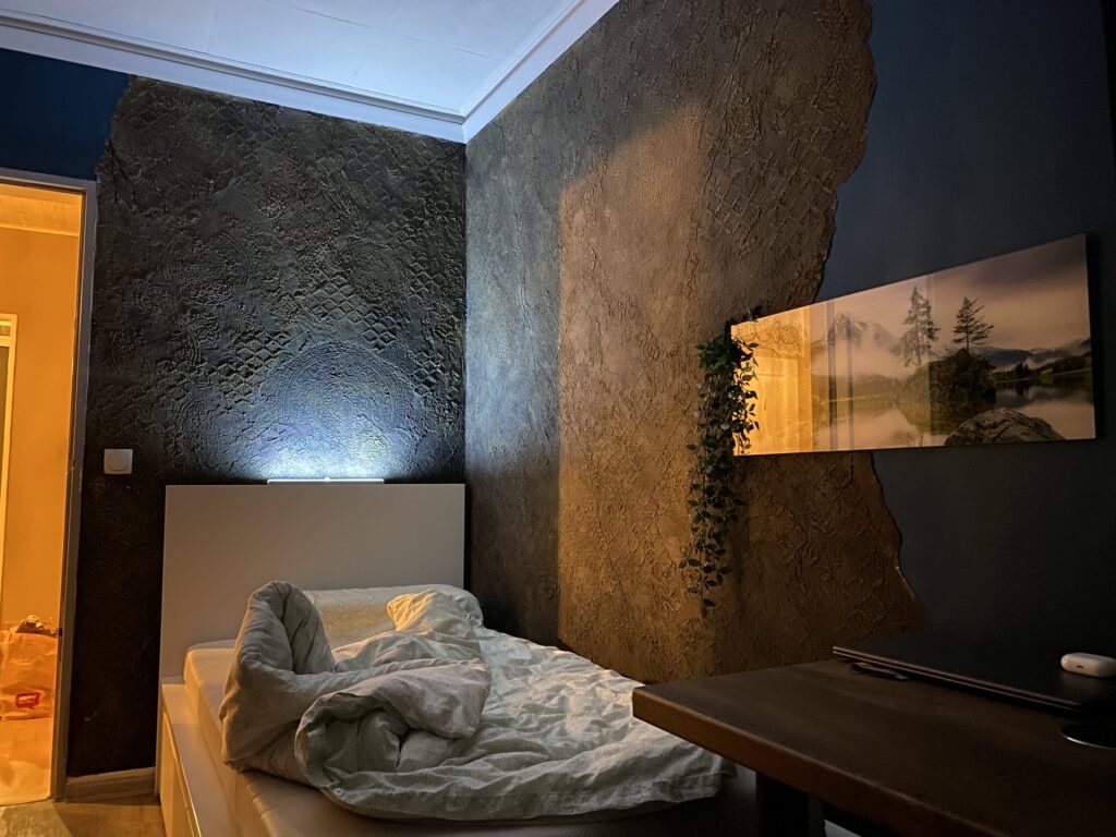 Schlafzimmer mit dunkler Kunststeinwand voller erhabener orientalischer Ornamente, Bett mit Licht und gemütlicher Beleuchtung.