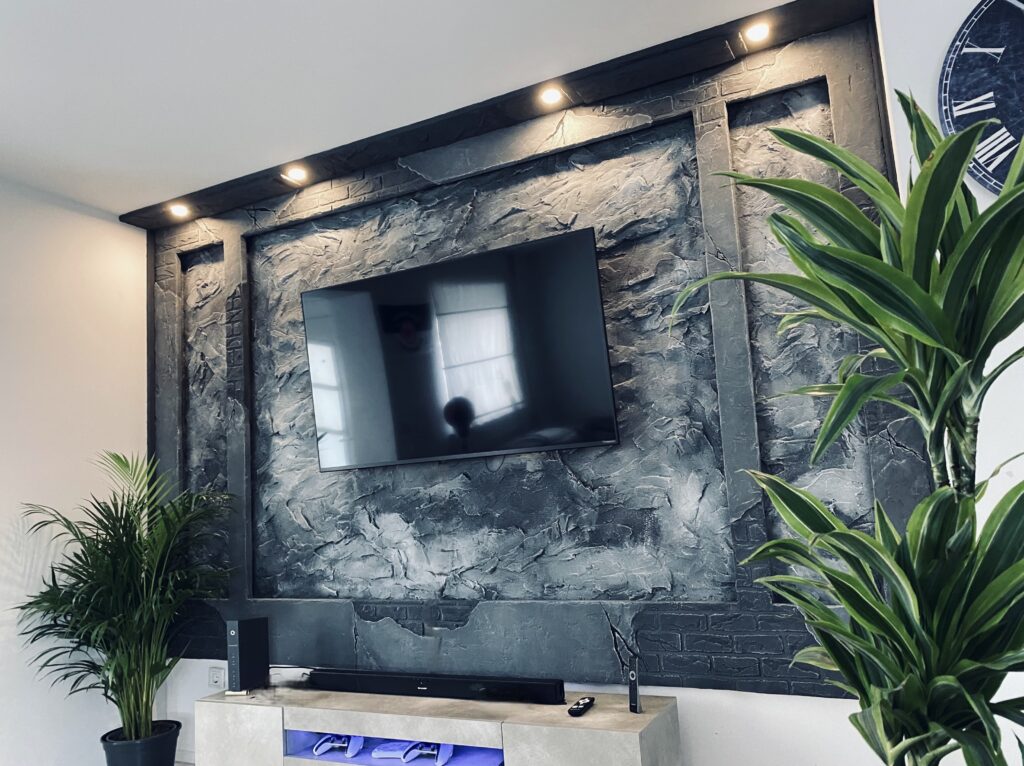 Moderne TV-Medienwand aus dunkelgrauem Kunststein mit Fels- und Ziegelstruktur, integrierter LED-Deckenbeleuchtung und montiertem Fernseher im Wohnzimmer.