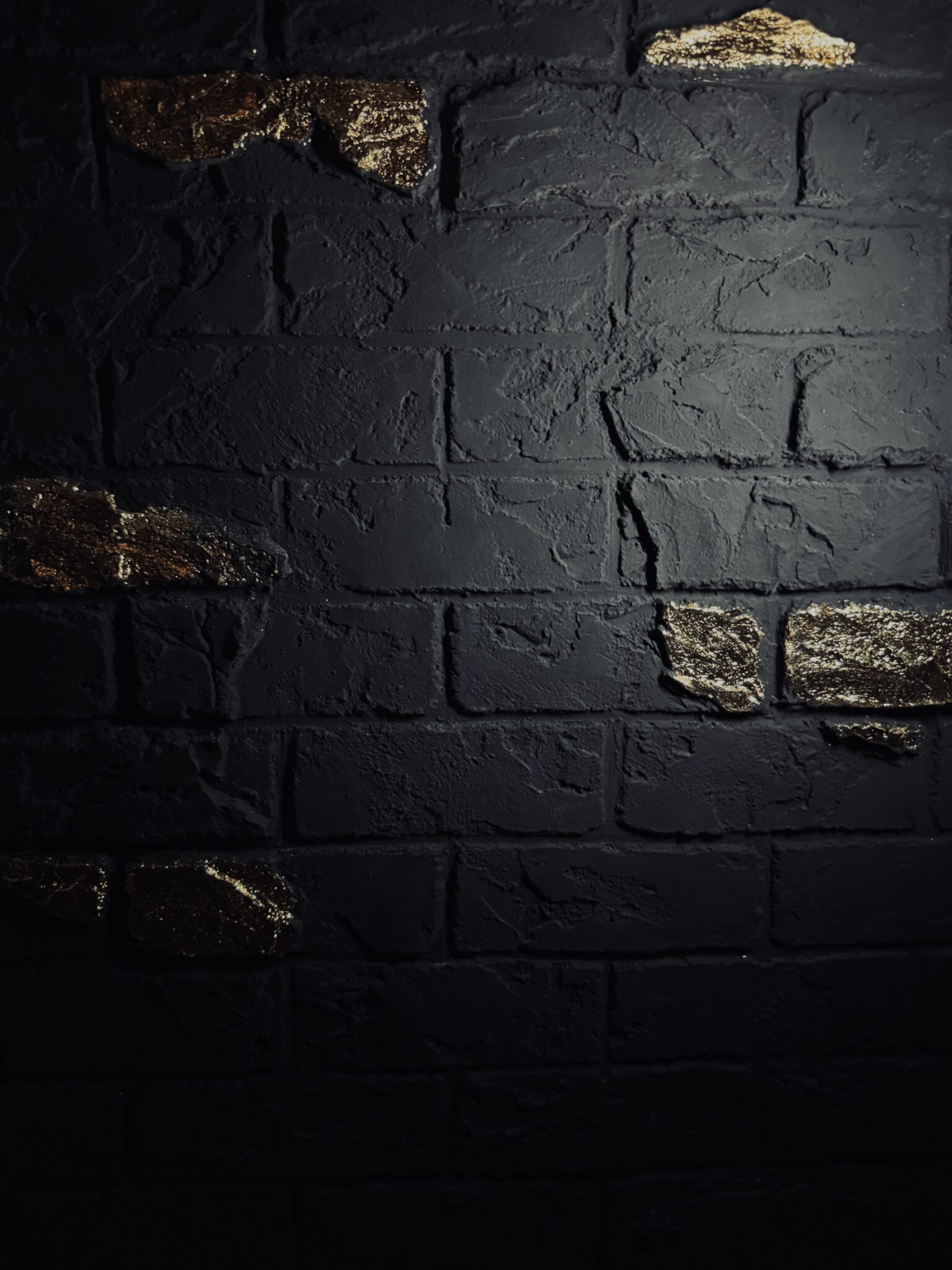 Detailaufnahme einer schwarzen Kunststein-Ziegelwand mit fühlbarer Textur und Blattgold-Azenten.
