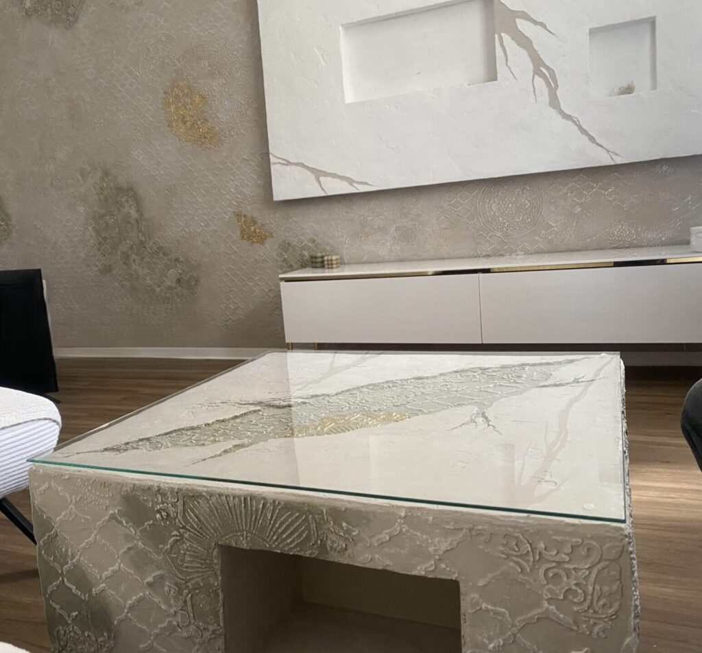Ganzheitlich gestaltetes Wohnzimmer mit strukturierter Kunststein-Wand, weißer vorgesetzter TV-Wand mit Nischen und farblich passendem Kunststein-Couchestisch mit Glasplatte.